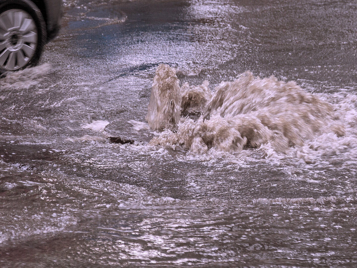 Wasser quillt aus dem Gullideckel infolge einer Kanalüberlastung durch Starkregen.